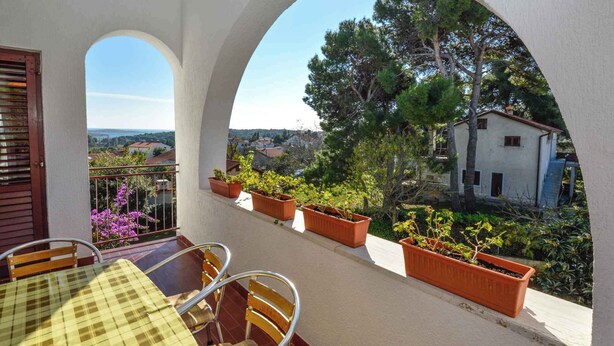 A balcony with a table and chairs, potted plants, and a view of a village. - Holiday apartment with air conditioning and balcony (Premantura)
