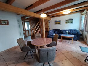 A cozy living room with a wooden ceiling, a blue sofa, a round table with chairs, and a staircase leading to another room. - A - Uns Schün, Germany (Middelhagen)