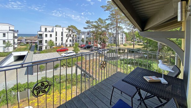 A balcony with a table and chairs, overlooking a street with parked cars and buildings.