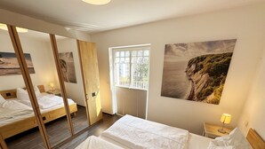 A bedroom with two beds, a window with blinds, a mirror, and a painting on the wall.