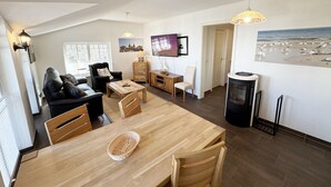 A spacious living area with a wooden dining table, a black sofa, a TV, and a fireplace.