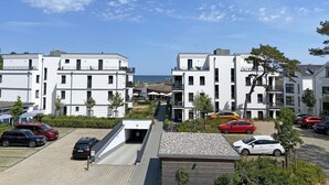 A residential area with modern white buildings, a covered parking area, and a view of the sea.