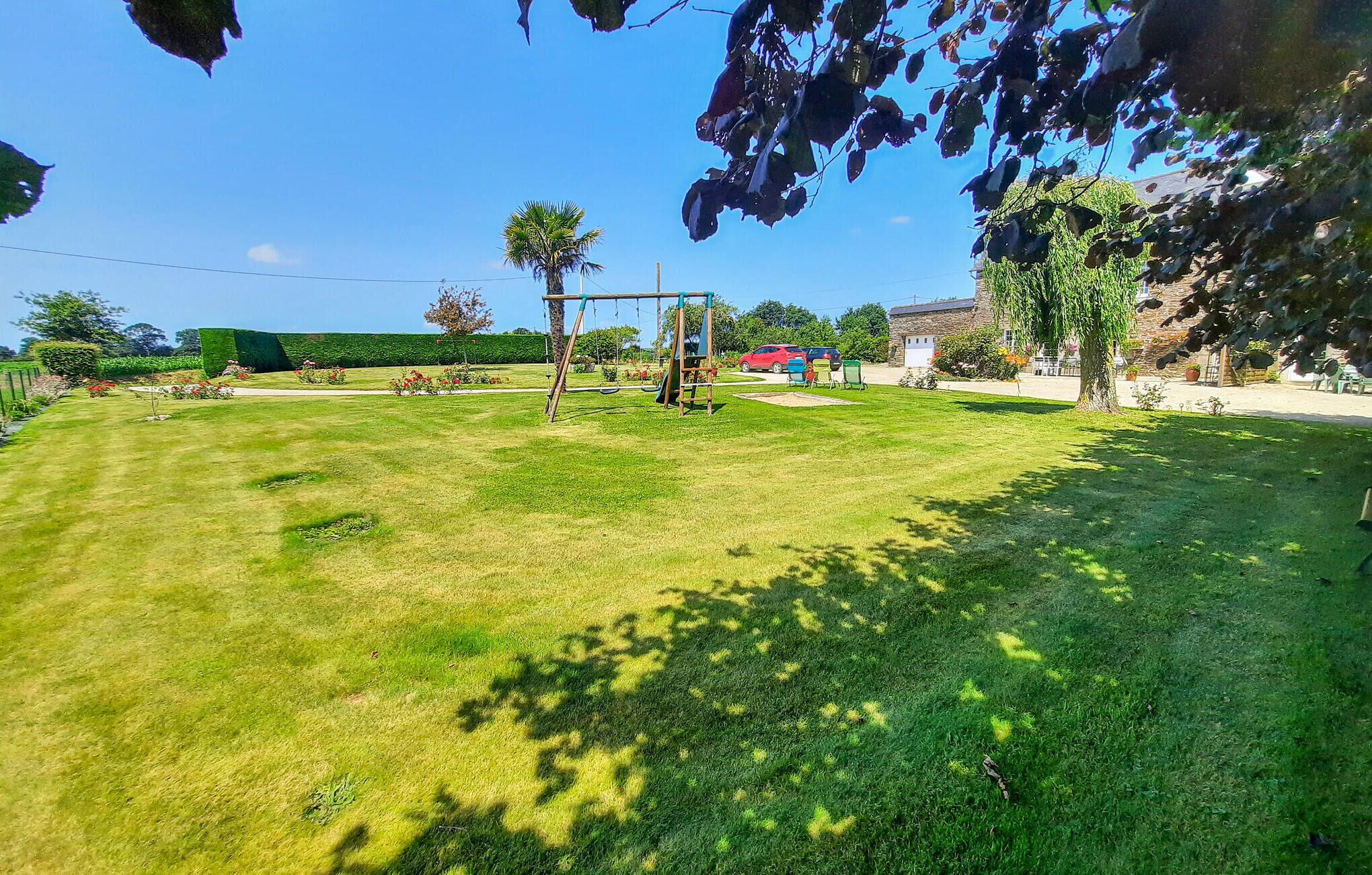 Un área verde bien cuidada con un columpio, un pequeño estanque y un edificio de piedra al fondo.