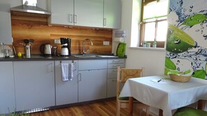 Une cuisine dotée d’un plan de travail en bois, d’une machine à café, d’une bouilloire et d’un évier. On y trouve également un coin repas avec une table et des chaises.