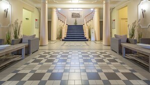 Un hall d’entrée avec un sol à carreaux, un escalier et deux espaces de détente agrémentés de plantes.