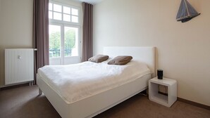 Une chambre à coucher avec un lit, un radiateur, une fenêtre avec des rideaux et un luminaire fixé au mur.