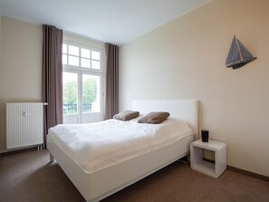 Ein Schlafzimmer mit Bett, Heizkörper, einem fenster mit Vorhängen und einer Wandleuchte.