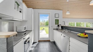 Une cuisine moderne avec des armoires blanches, un four à micro-ondes encastré, un évier et une fenêtre donnant sur un jardin.