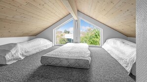 Une chambre avec un plafond en pente, deux lits, une grande fenêtre et une vue sur les arbres.