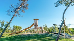 Un parque infantil con tobogán y estructuras para escalar, rodeado de árboles y césped.