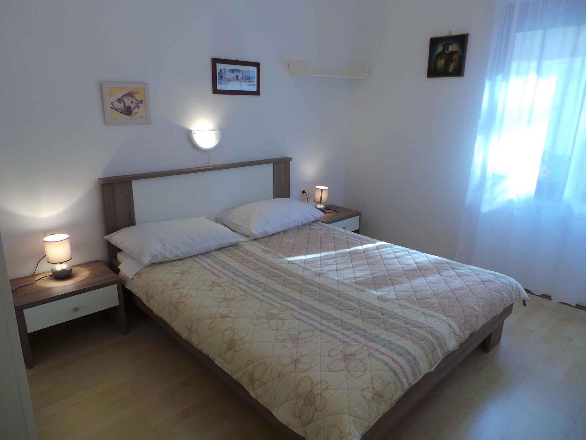 Ein Schlafzimmer mit einem Bett, zwei Nachttischen, einer Wandleuchte und einem Fenster mit Vorhängen.