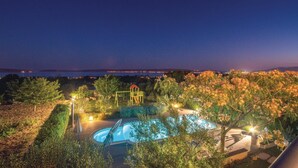 A swimming pool surrounded by trees and a playground, with a view of the sea at dusk. - Gorgeous apartment in Kastel Luksic (Kastel Luksic)