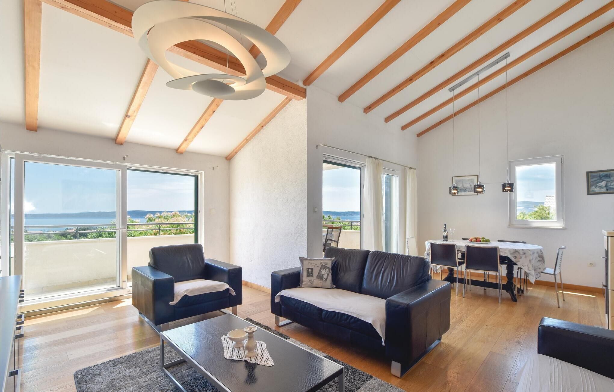 A spacious living area with a modern design, featuring a sofa, armchairs, a dining table, and a view of the outdoors.