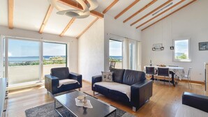 Een ruime woonkamer met een modern design, met een bank, fauteuils, een eettafel en uitzicht op het omliggende landschap.