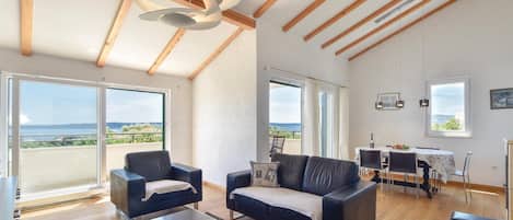 A spacious living area with a modern design, featuring a sofa, armchairs, a dining table, and a view of the outdoors.