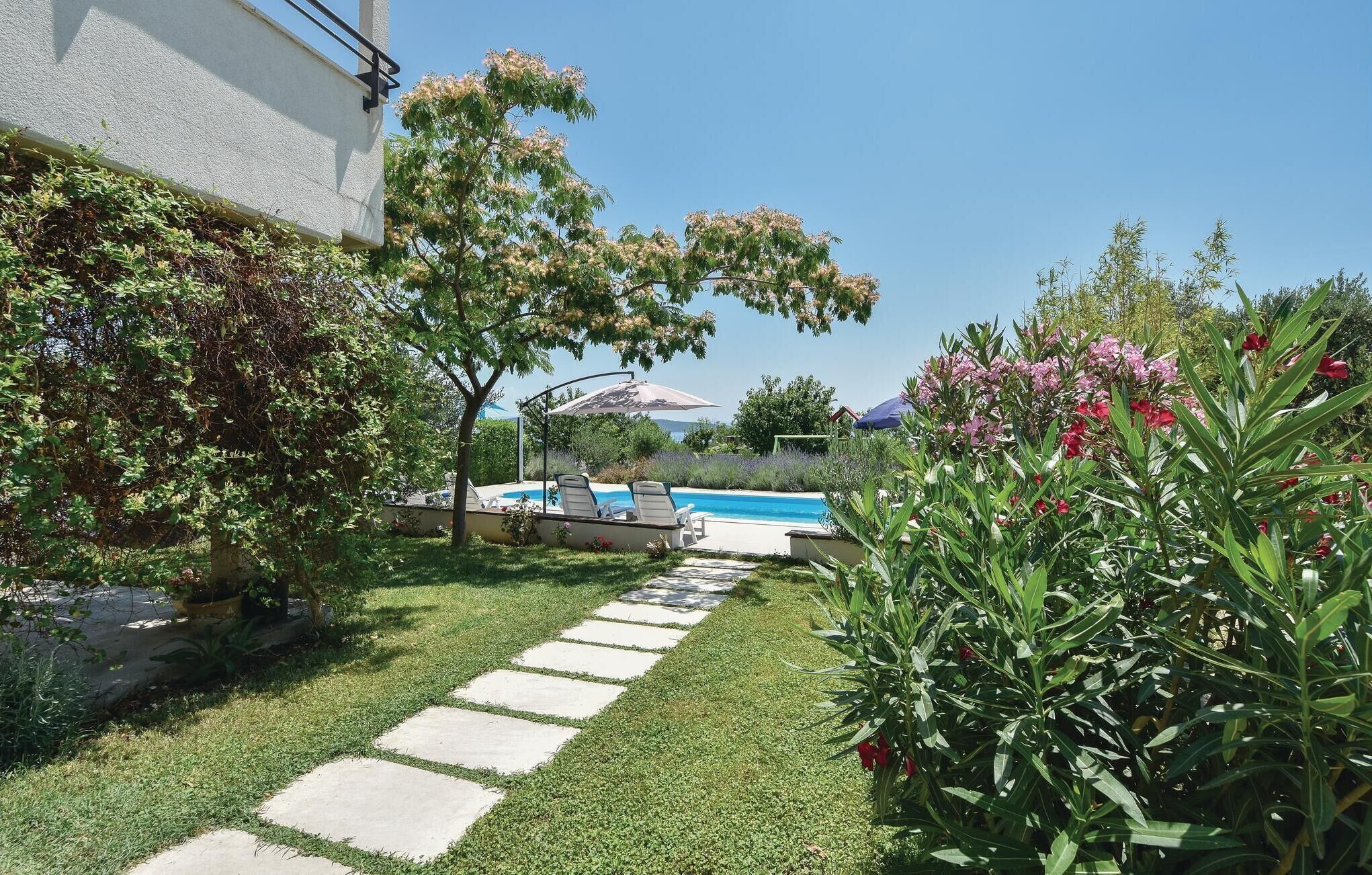 En baghave med swimmingpool, en brostenssti og forskellige planter.