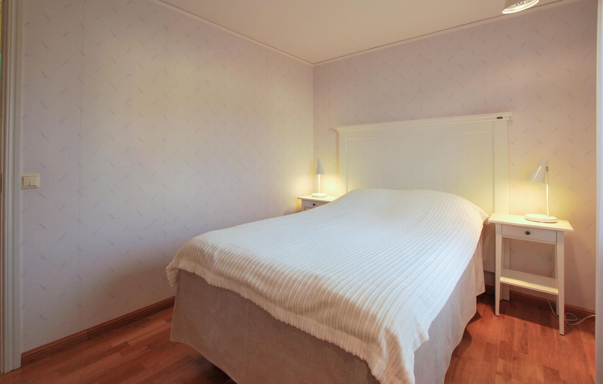 A bedroom with a single bed, two bedside tables with lamps, and a wooden floor.