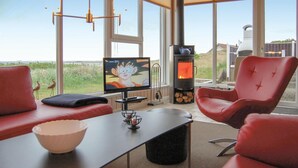 A modern living room with a television, red chairs, a table with a bowl, and a wood-burning stove.