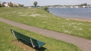 Un espace verdoyant avec un sentier et un banc, offrant une vue sur une étendue d’eau où se trouvent des bateaux.