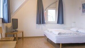 Une chambre à coucher avec un lit, un bureau avec un ordinateur, une chaise et une fenêtre avec des rideaux.