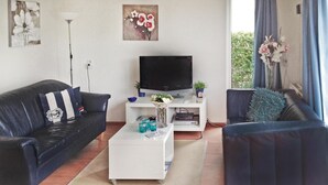 Un salon avec un canapé en cuir noir, une table basse blanche, un téléviseur à écran plat et une petite table d’appoint blanche.