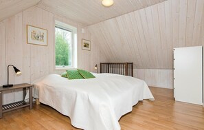 A bedroom with a bed, a bedside table, a lamp, a window, and a door.