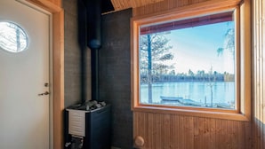 Ett rum med en vedeldad kamin, ett fönster med utsikt över en sjö och en dörr med ett runt fönster.