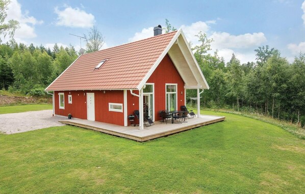 A red single-story house with a sloped roof, a porch with outdoor seating, and a small deck.