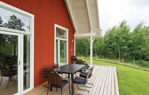 An outdoor deck with a table and chairs, a pergola, and a view of a green landscape.
