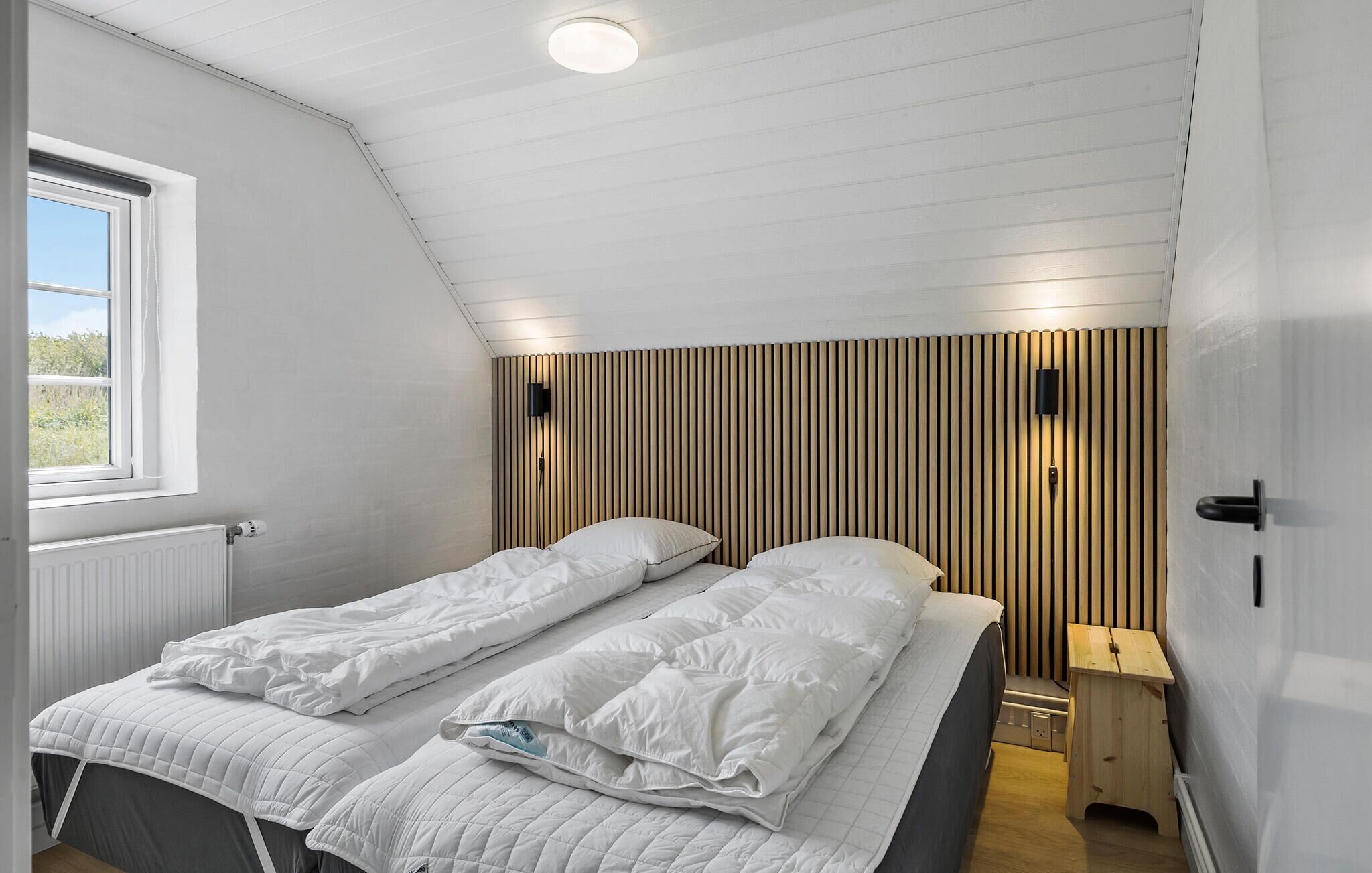 A single bed with white bedding in a room with a sloped ceiling and wooden panel wall.