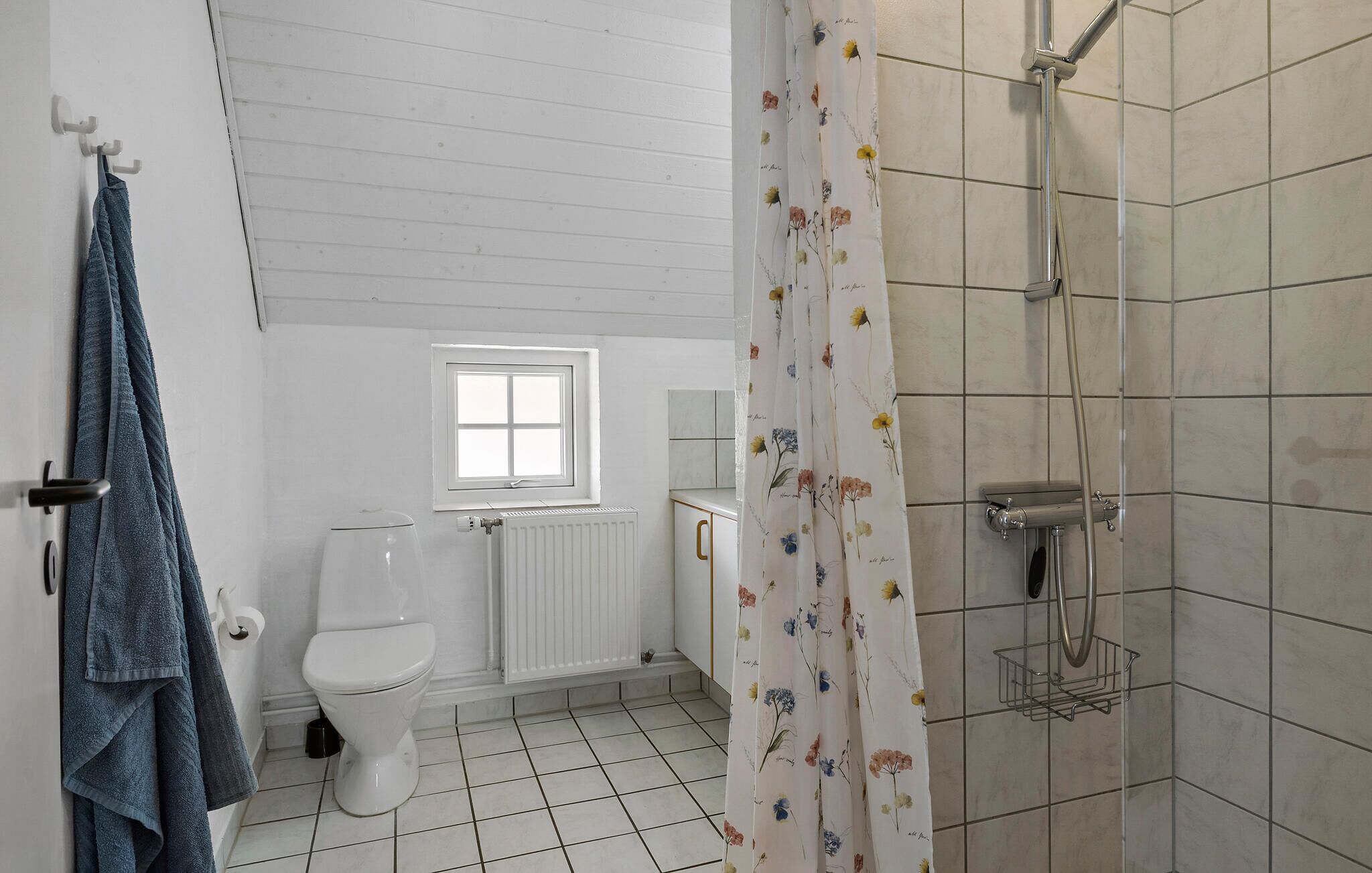 Une salle de bain avec des toilettes, une fenêtre, une douche avec un rideau et des serviettes suspendues sur un porte-serviettes.