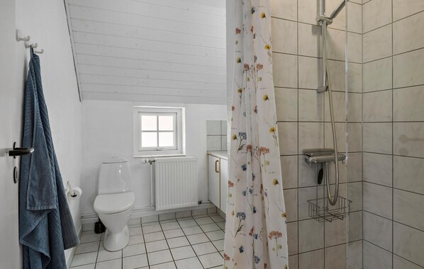 A bathroom with a toilet, a window, a shower with a curtain, and towels hanging on a rack. - Awesome home in Ulfborg with kitchen (Ulfborg)