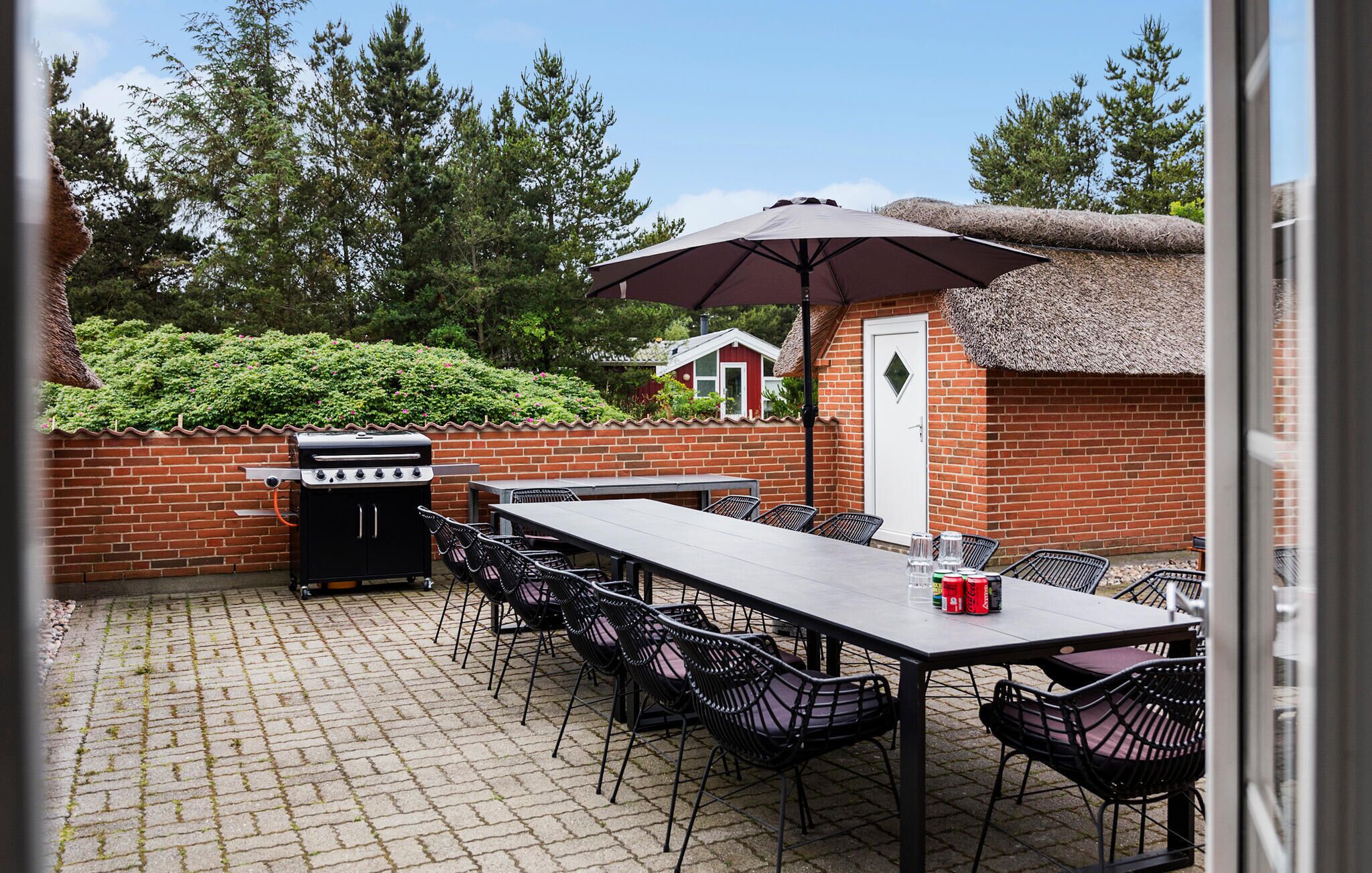 An outdoor patio with a brick wall, a grill, a table with chairs, and a thatched-roof structure.