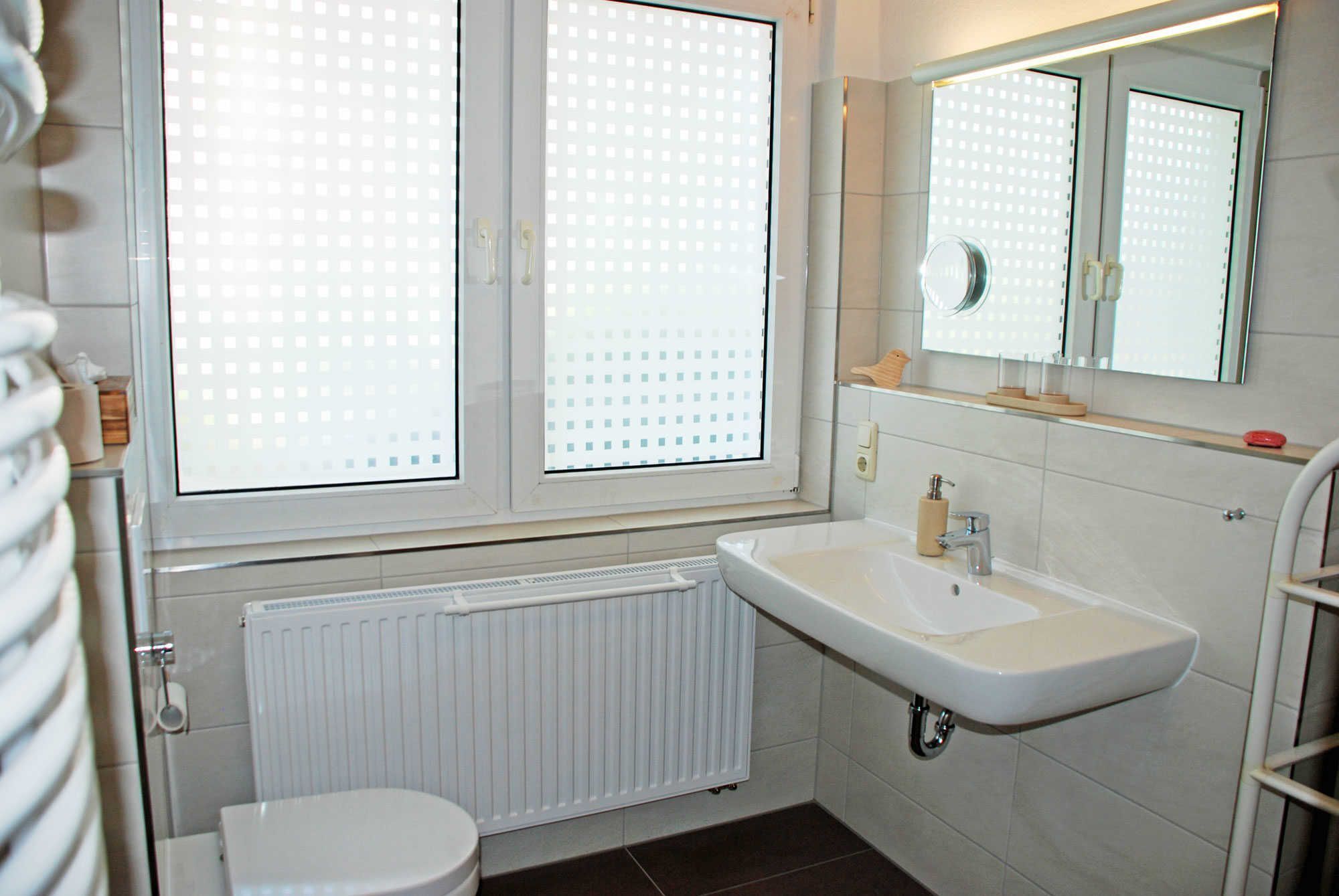Ein Badezimmer mit Toilette, Waschbecken, Spiegel und einem Fenster mit Jalousien.