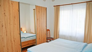 Ein Schlafzimmer mit einem Holzschrank, einem Bett mit blauer Bettwäsche, einem Stuhl und einem großen Spiegel.