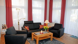 Ein Wohnzimmer mit zwei schwarzen Sofas, einem Holztisch und einem roten Teppich mit Muster.