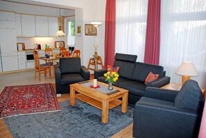 A modern living room with a sofa, armchairs, a coffee table, and a dining area with chairs and a table.