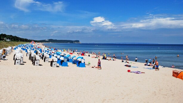 Ein Strand mit Reihen Zelte und Liegestühle, ein sandiger Uferstreifen und das Meer im Hintergrund.