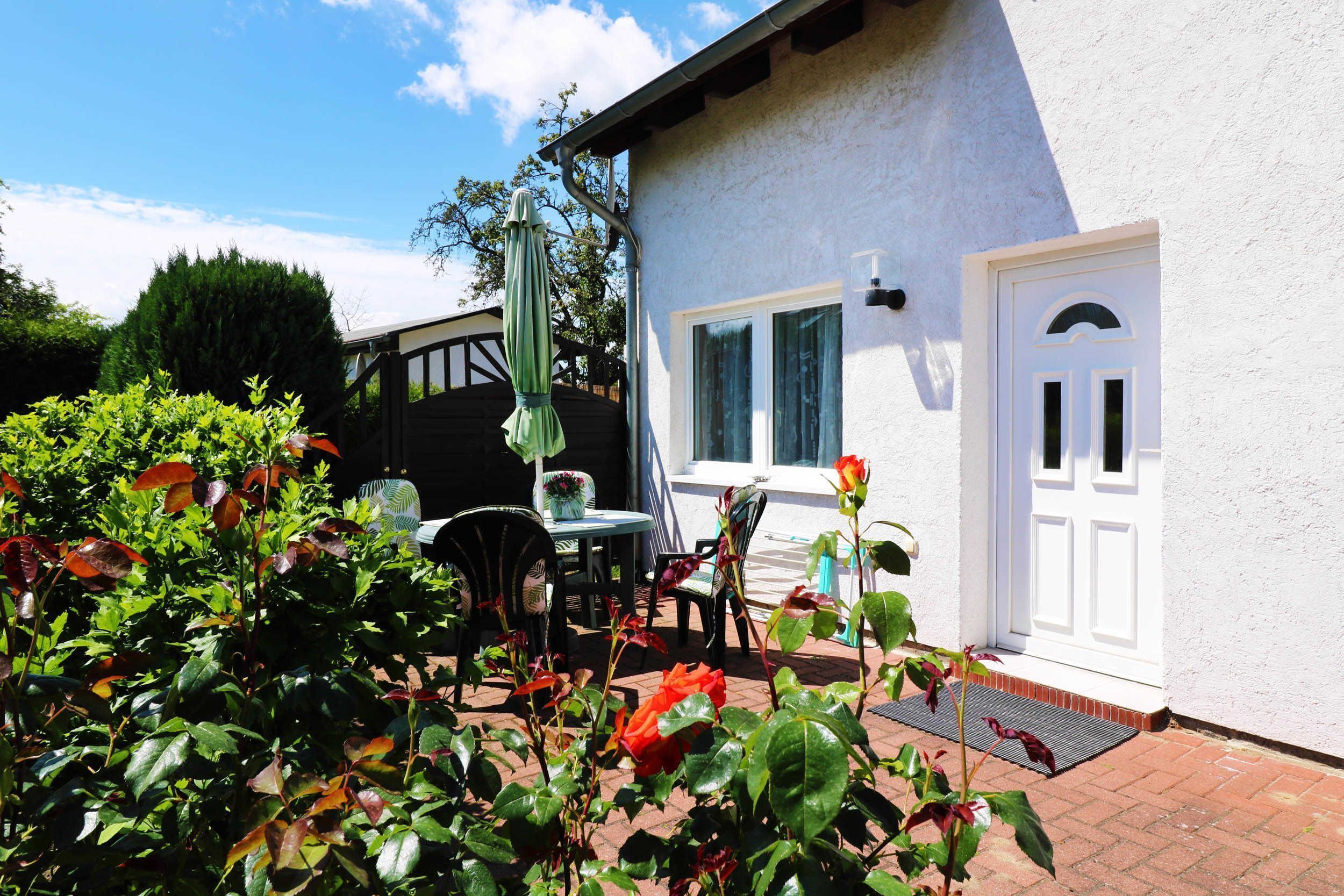 Un patio con mesa y sillas, una puerta blanca y un jardín lleno de rosas.