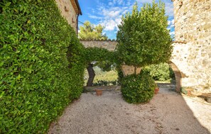A courtyard with a gravel path, stone walls, and lush greenery. - Luxurious home in Petroro Todi PG (Petroro Todi PG)