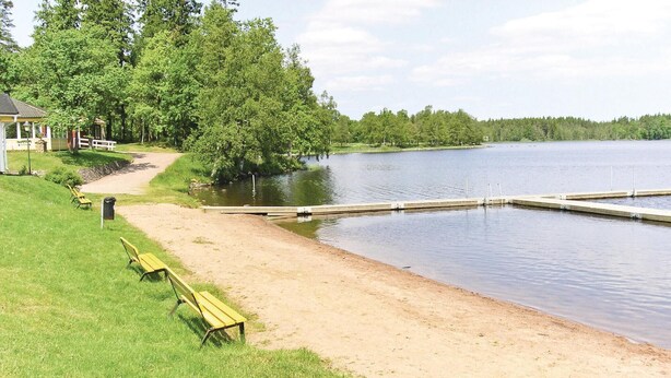 Un parc au bord du lac, avec une plage de sable, une jetée en bois et une rangée de bancs jaunes.