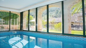 Une piscine intérieure offrant une vue dégagée sur un jardin et un bâtiment doté d’un toit en tuiles.