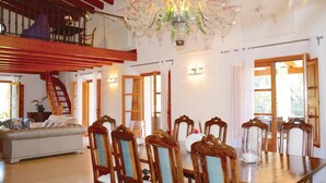 Un espace repas avec une table et des chaises en bois, un lustre et un escalier menant à un niveau supérieur.