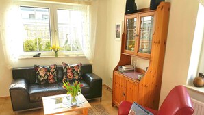 A living room with a black leather sofa, a wooden coffee table, a red armchair, and a wooden cabinet with glass doors.