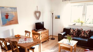 A living room with a wooden dining table, chairs, a sofa, a TV, and a floor lamp.