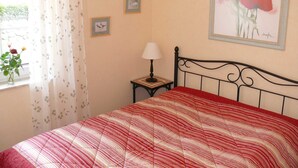 A bedroom with a bed, a window with curtains, a lamp, and wall art.