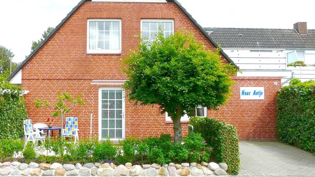 A red brick house with a gabled roof, two windows, and a sign reading 'Haus Antje.'