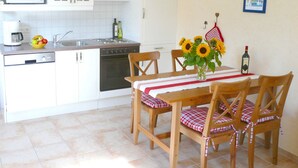 A kitchen with white cabinets, a microwave, a sink, and a dining table with checkered tablecloths and wooden chairs.