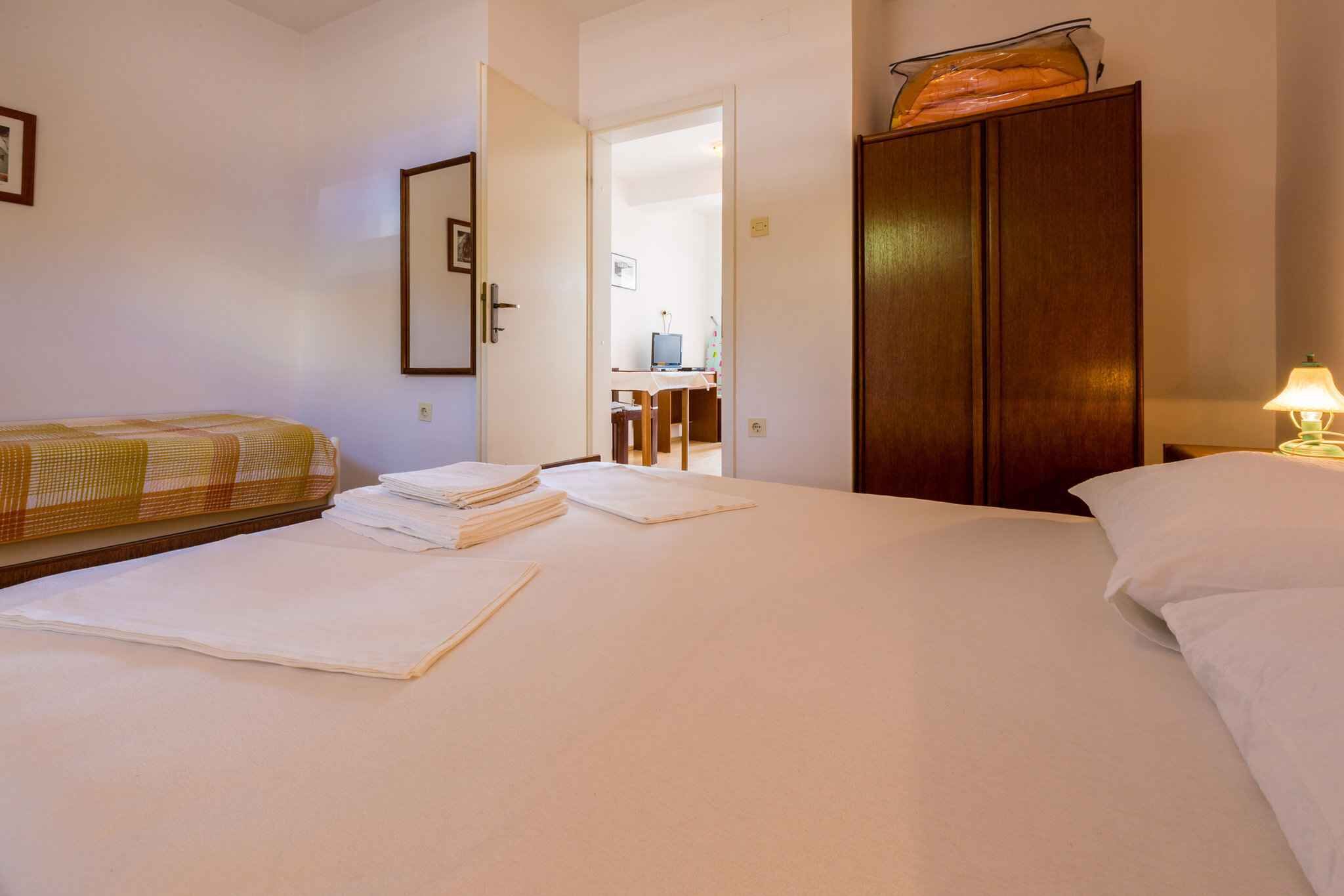 A hotel room with a bed, a wardrobe, a desk with a computer, and a lamp.