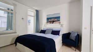 Une chambre à coucher avec un lit, une chaise, une fenêtre et un tableau accroché au mur.